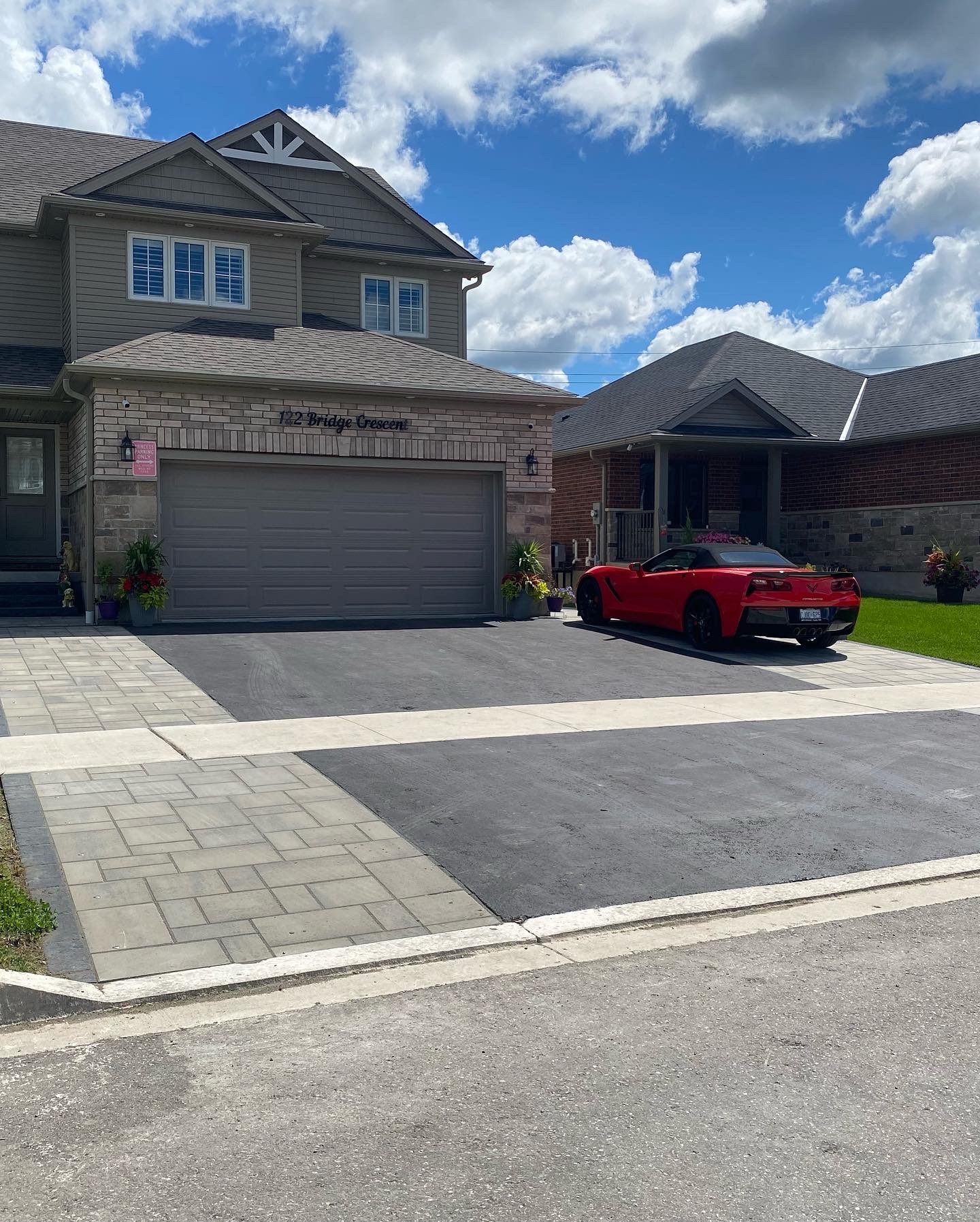 A suburban two-story house with a gray garage and a red sports car parked in the driveway under a partly cloudy sky.