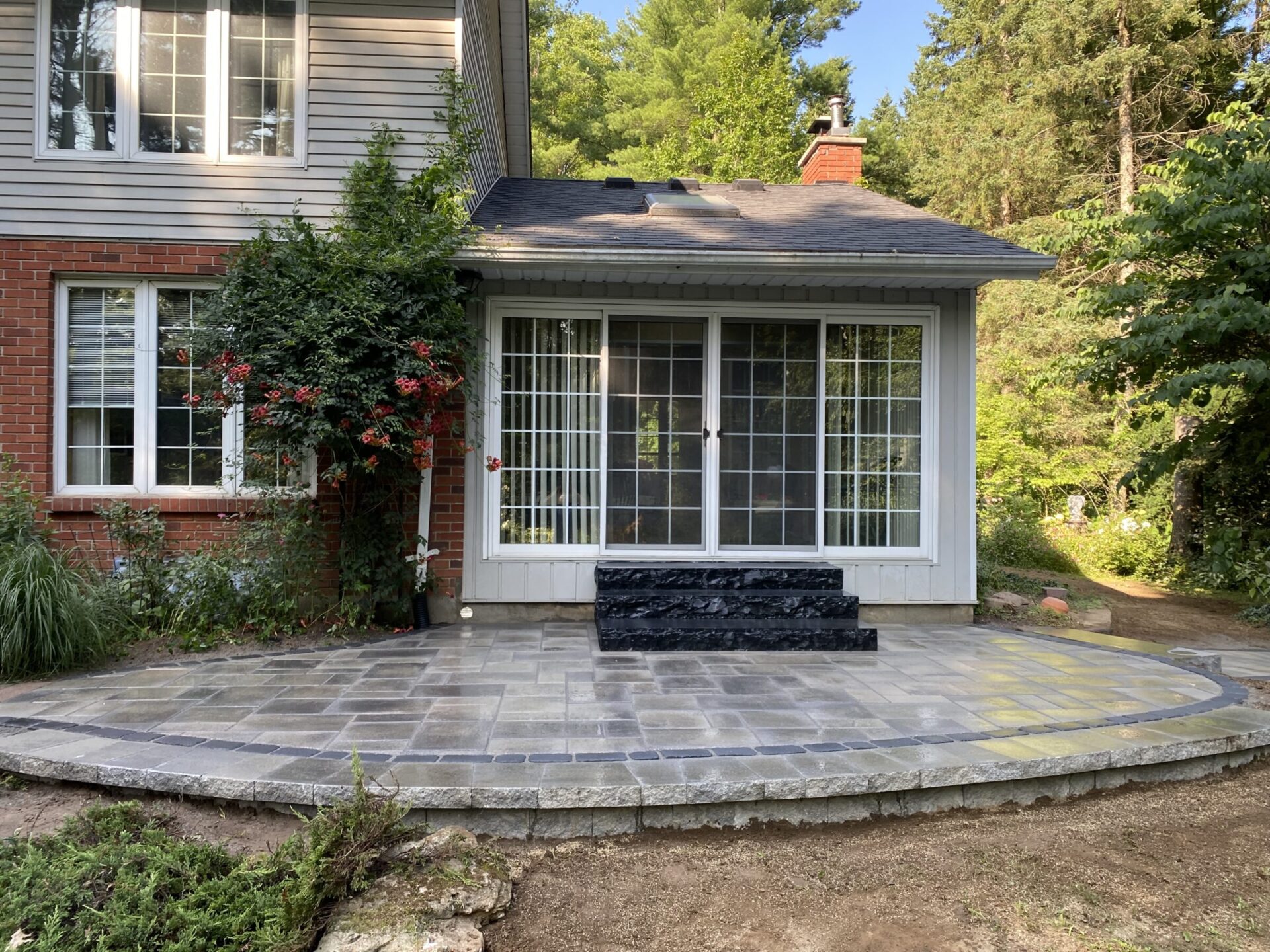 A cozy house with a brick and siding exterior, featuring a sunroom with large glass doors, surrounded by trees and greenery.