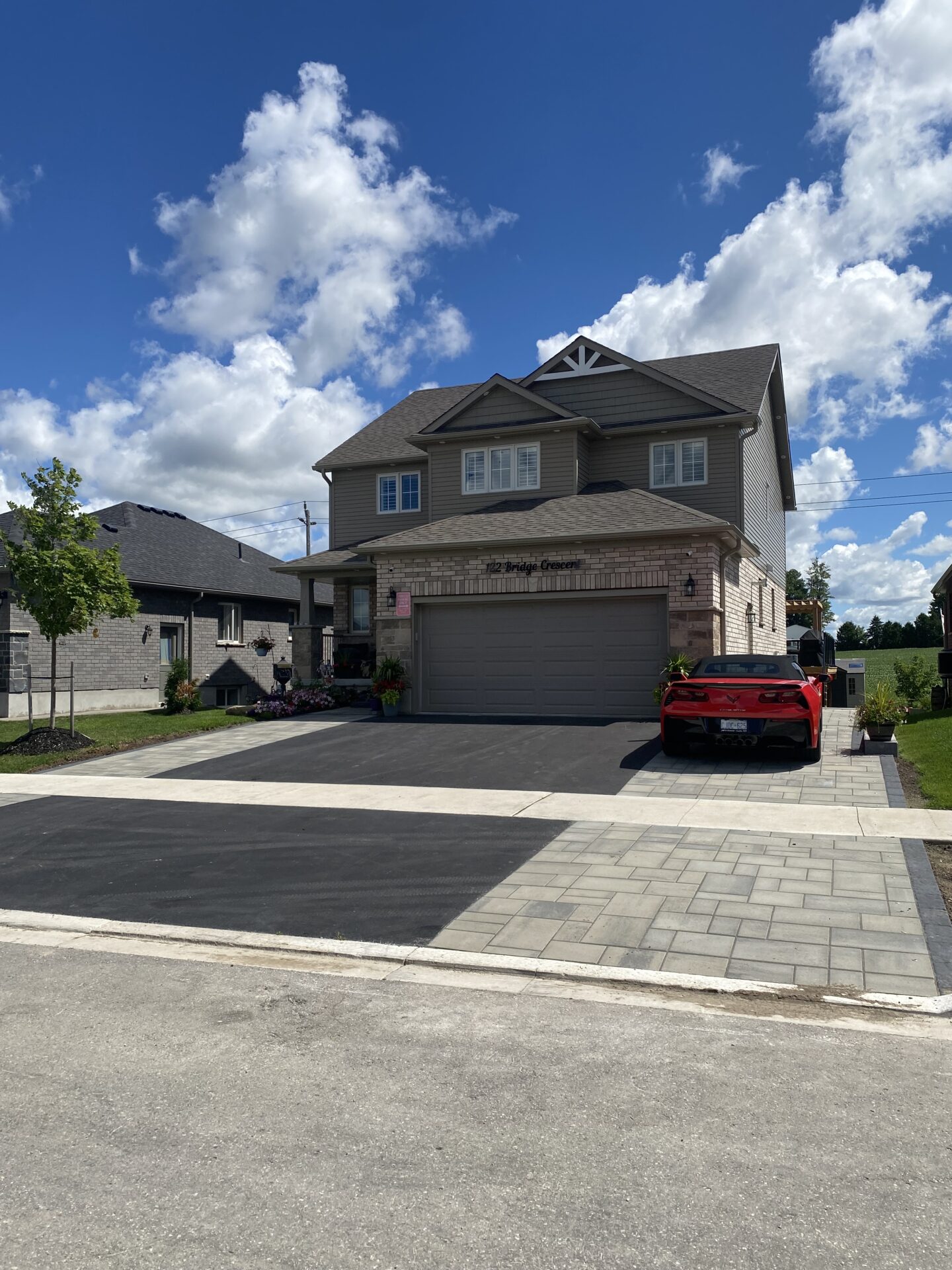 A modern two-story house with a red car in the driveway under a bright blue sky with fluffy clouds.