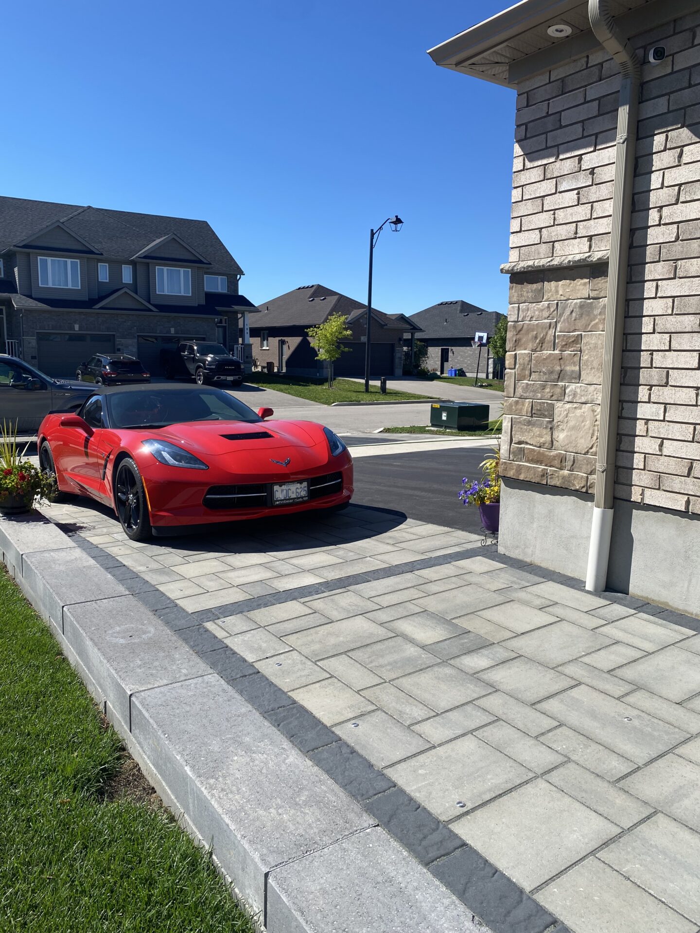 A red sports car parked on a residential driveway, surrounded by modern suburban houses, under a clear blue sky on a quiet street.