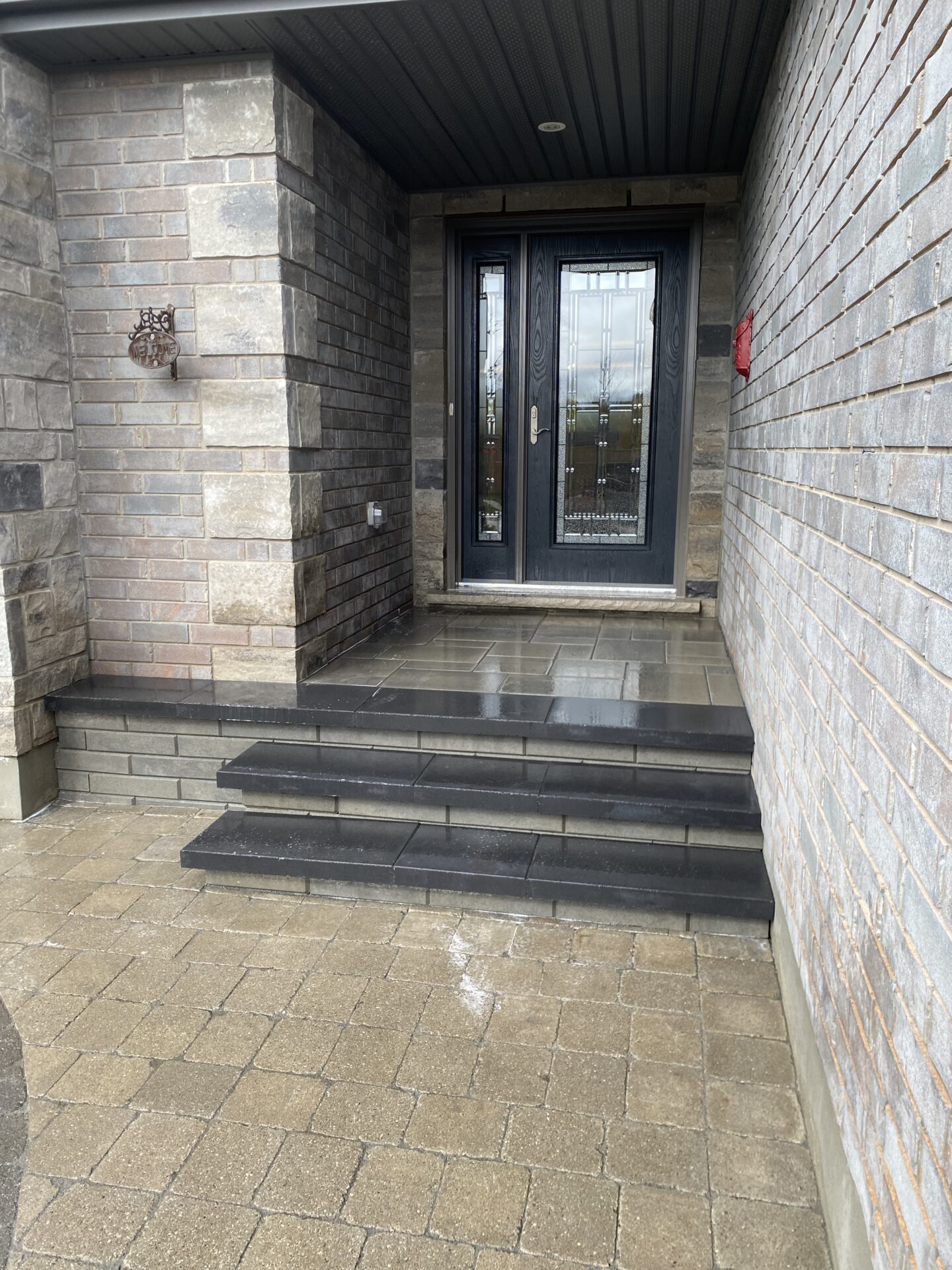 Elevated entrance with stone steps leads to a modern double door under a covered porch, featuring sleek brickwork and minimalist design elements.