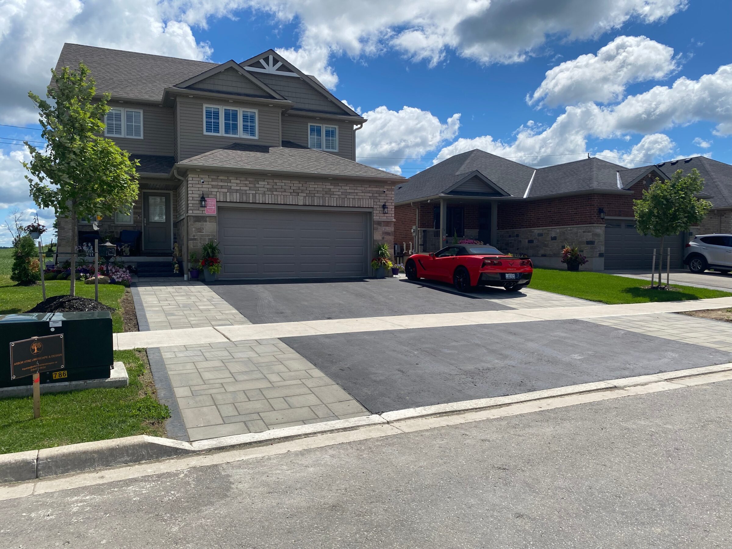A suburban neighborhood with two houses, red convertible parked in driveway, neatly manicured lawns, and a partly cloudy sky.