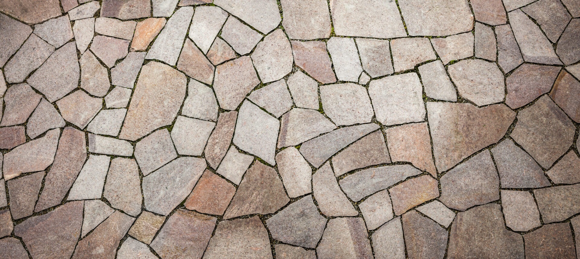 Irregular stone paving pattern forms an abstract mosaic. Natural shades of beige and pink create a textured surface, hinting at rustic pathways.